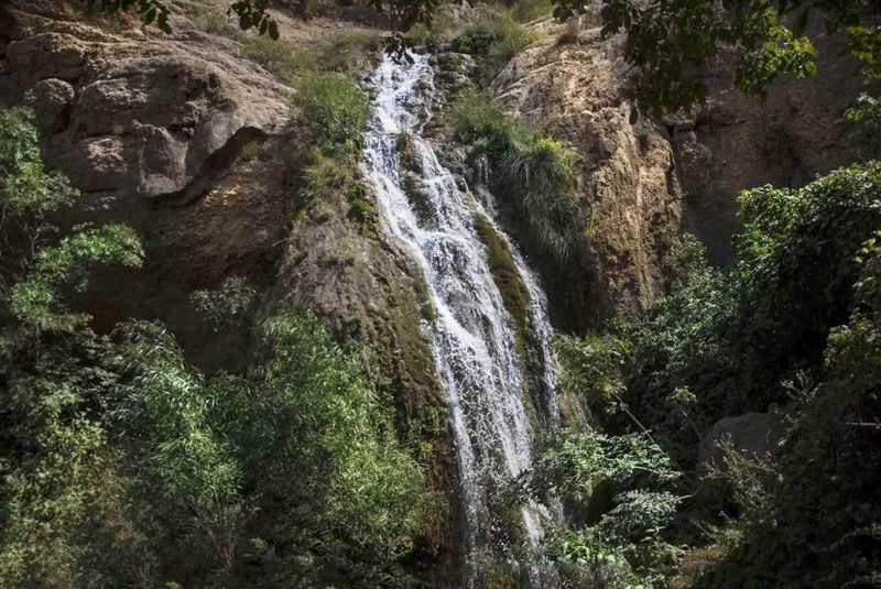 آبشار آبگرم در حال گذر از میان صخره ها و درختان 