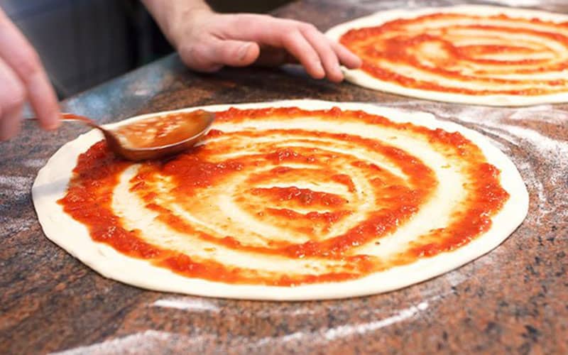 ریختن سس گوجه روی خمیر پیتزا