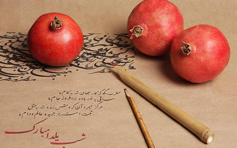 چند انار و قلم خوشنویسی روی صفحه ای با عنوان شب یلدا