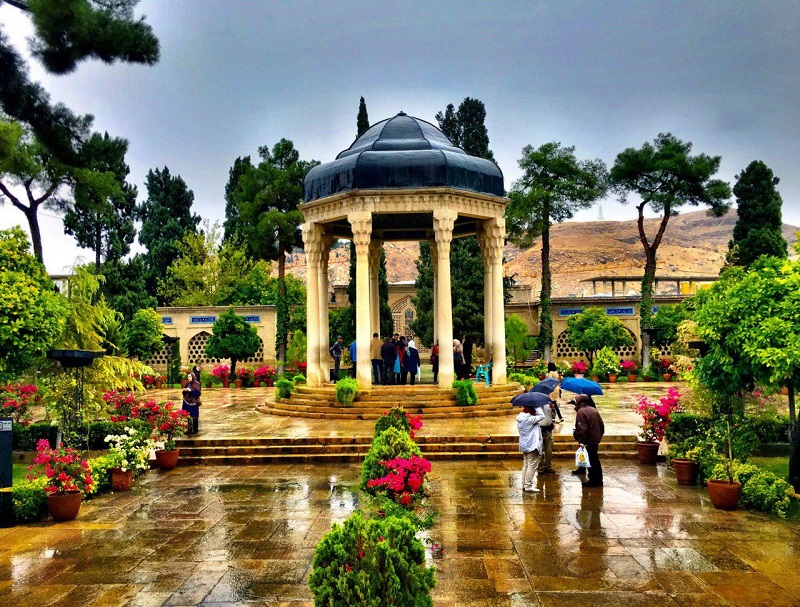 منظره بارانی و گردشگران با چتر در حیاط حافظیه