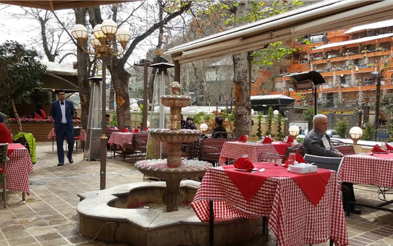 رستورانی با میزهای در فضای باز و آبنما