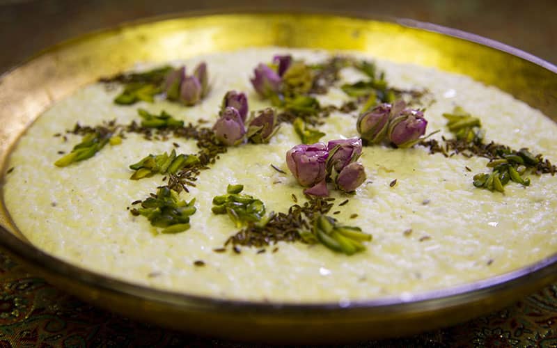 یک ظرف شیر برنج با تزیین گل محمدی و خلال پسته