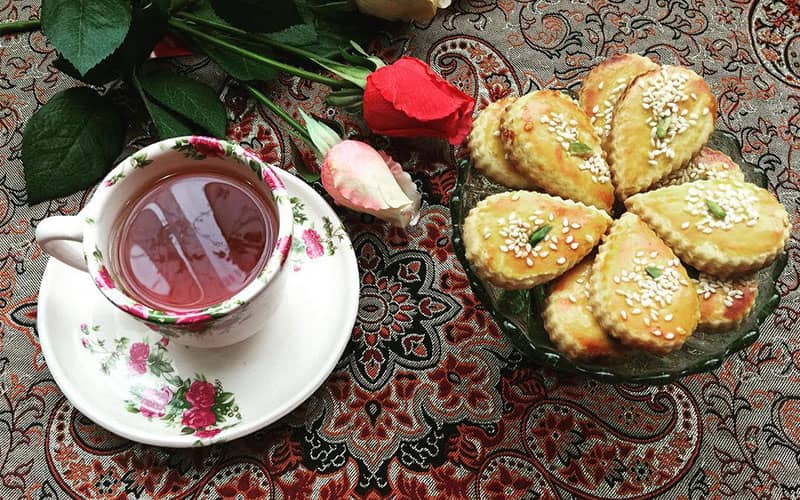 یک ظرف شیرینی با یک فنجان چای و دو شاخه گل رز