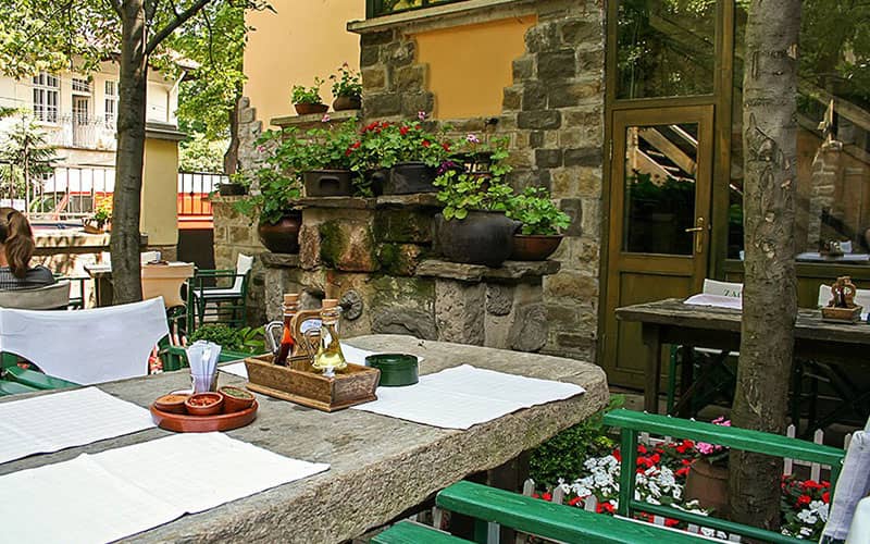 رستورانی در فضای باز با نیمکت سنگی و صندلی های سبز رنگ