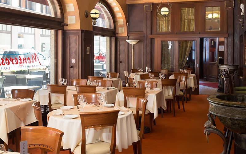 رستورانی با پنجره های بزرگ و کفپوش قهوه ای و تعداد زیادی لیوان روی میزها