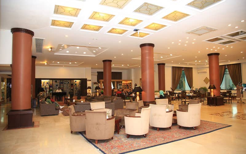 لابی بزرگ یک هتل با چندین ستون قهوه ای رنگ و پیانویی در گوشه آن