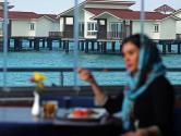 خانمی مشغول صرف غذا رستوران با چشم اندازی به دریا و کلبه هایی که روی دریا ساخته شده
