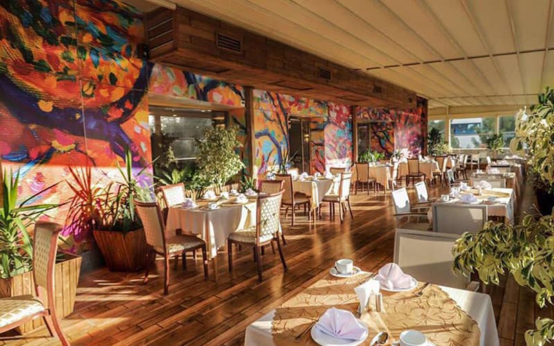 رستورانی با کف پارکت و صندلی های چوبی و دیواری با نقاشی رنگ و روغن