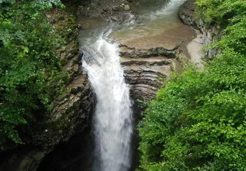 آبشار ویسادار سرازیر شده از صخره‌های لایه‌ایدر کنار درختان سبز