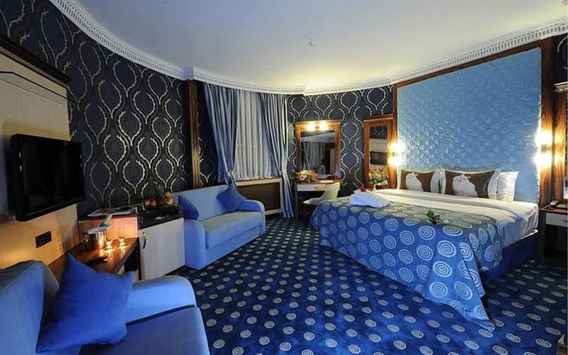اتاقی با دکوراسیون آبی و یک تخت دونفره و دو مبل یک نفره