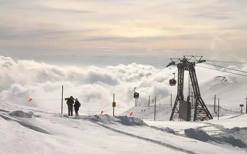 تله کابین و کوهنوردها در بالای قله کوه پر از برف و ابر