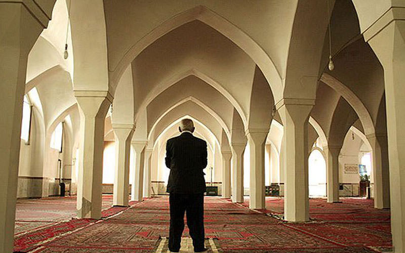مردی در حال خواندن نماز در مسجدی با ستون های زیاد