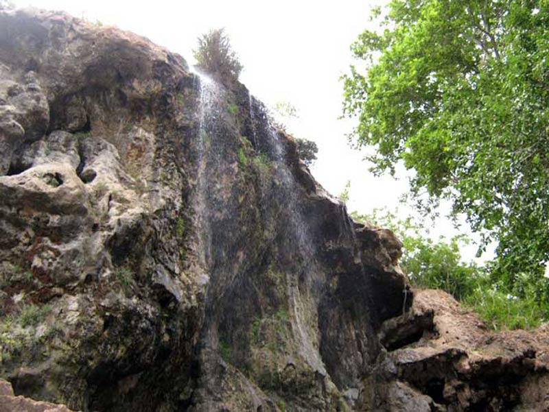 آبشار کمرد میان صخره های کوه و کنار درختان سبز