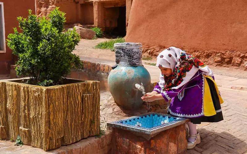 کودکی با لباس سنتی مشغول خوردن آب