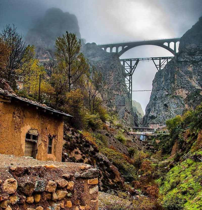 نمایی از پل در مسیر راه آهن سراسری ایران در جنگل سبز با خانه روستایی