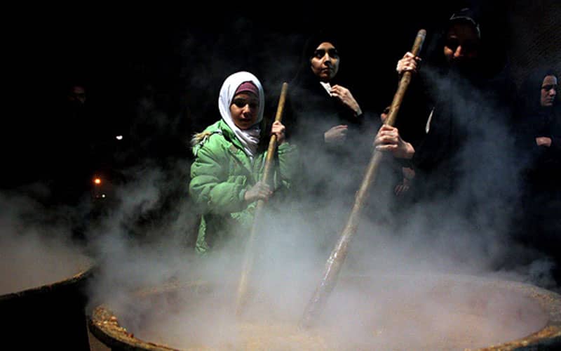 زنان مشغول همزدن دیگ نذری در شب