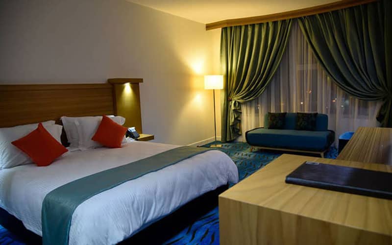 تخت دونفره با مبلمان آبی و پرده سبز در اتاق هتل