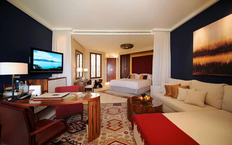 اتاق بزرگ هتل با مبلمان و تخت و تم رنگی قرمز و قهوه ای