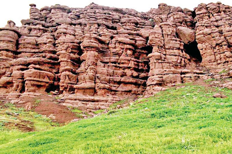 صخره های بلند تراشیده کنار چمنزار در دره هفت غار نیشابور