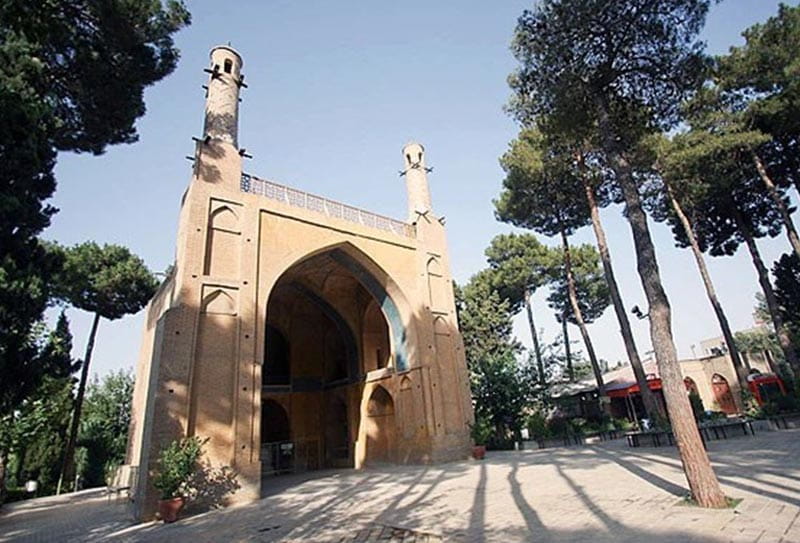 ساختمان منارجنبان در اصفهان کنار درختان و زیر آسمان آبی از نمای پایین