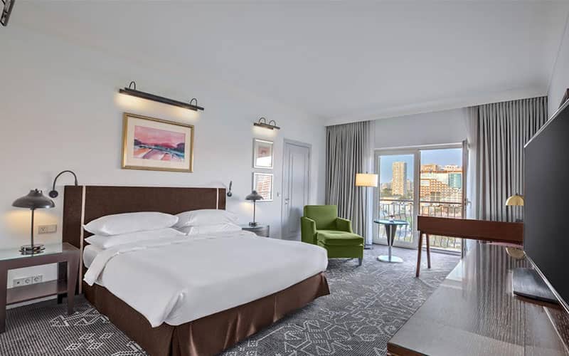 تخت دونفره و میز تحریر در اتاق هتلی مشرف به چشم انداز شهر