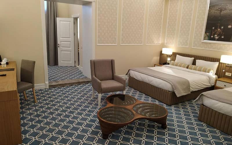 تخت دو نفره و مبلمان خاکستری در اتاق بزرگ هتل