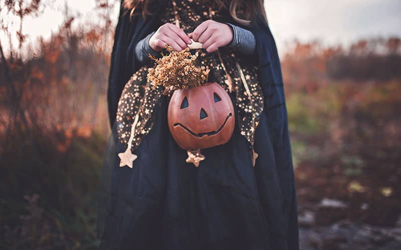 زنی با شنل سیاه و کدوتنبل هالووین در دست