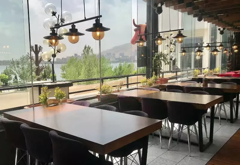 رستورانی مشرف به دریاچه با میزهای چوبی و لوسترهای سه تایی