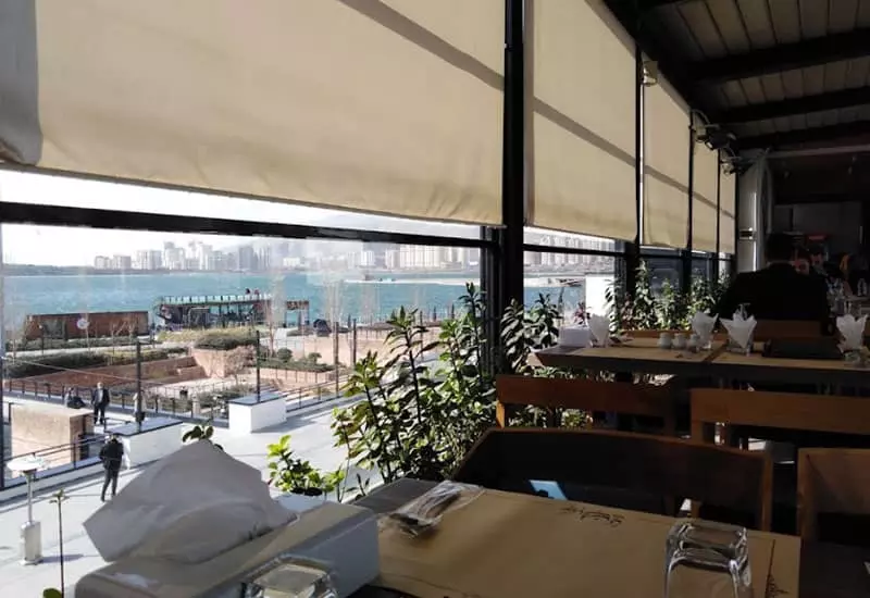 میز و صندلی های رستوران در کنار پنجره های بلند رو به دریاچه