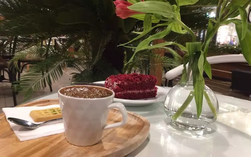 یک فنجان قهوه و کیک ردولوت در کنار گلدانی زیبا
