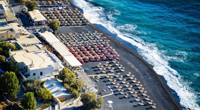 ساحل گردشگری کمری با تخت های رو به آفتاب در سانتورینی از نمای دور