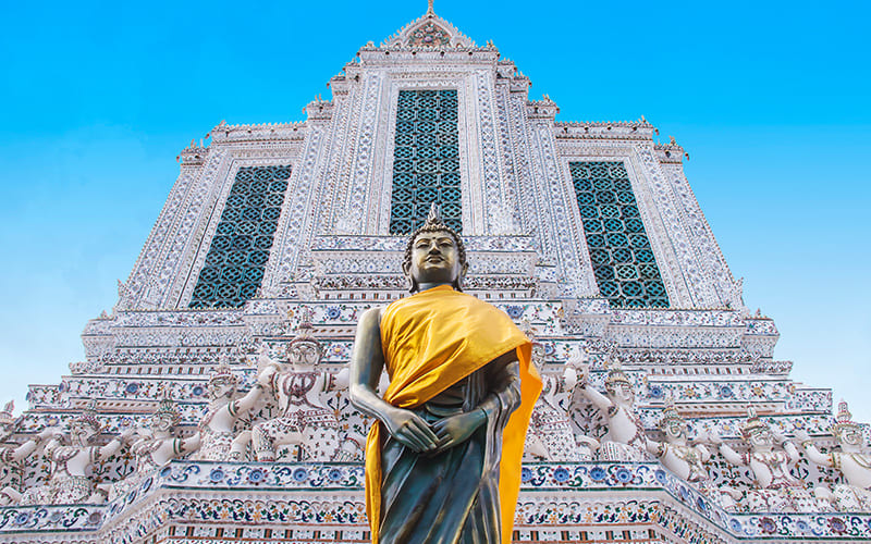 مجسمه بودای ایستاده در مقابل ساختمانی سفید در تایلند