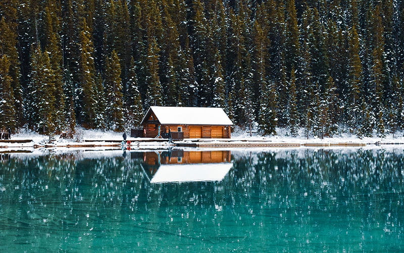 کلبه ای چوبی در کنار دریاچه و جنگل در زیر برف