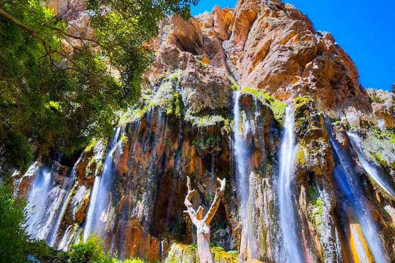 آبشار مارگون روی صخره بلند کنار درختان سبز از نمای پایین