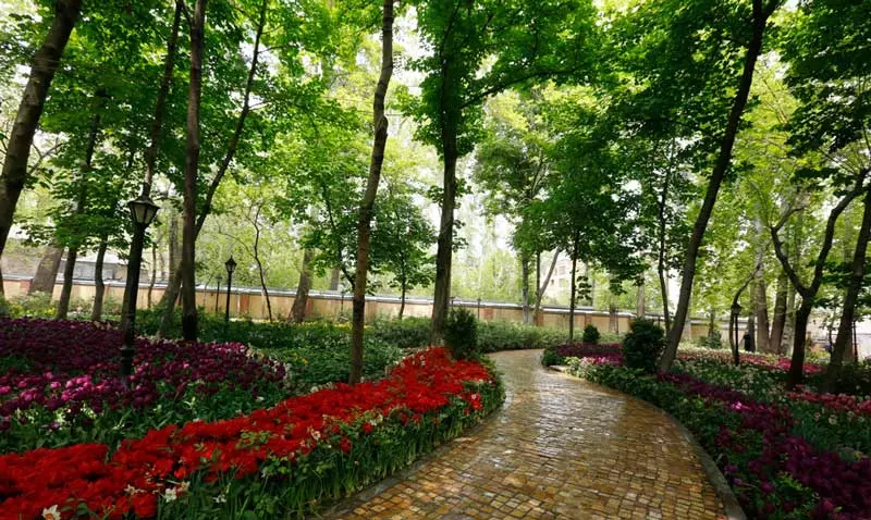 باغ ایرانی تهران با گل های قرمز و مسیر سنگفرش