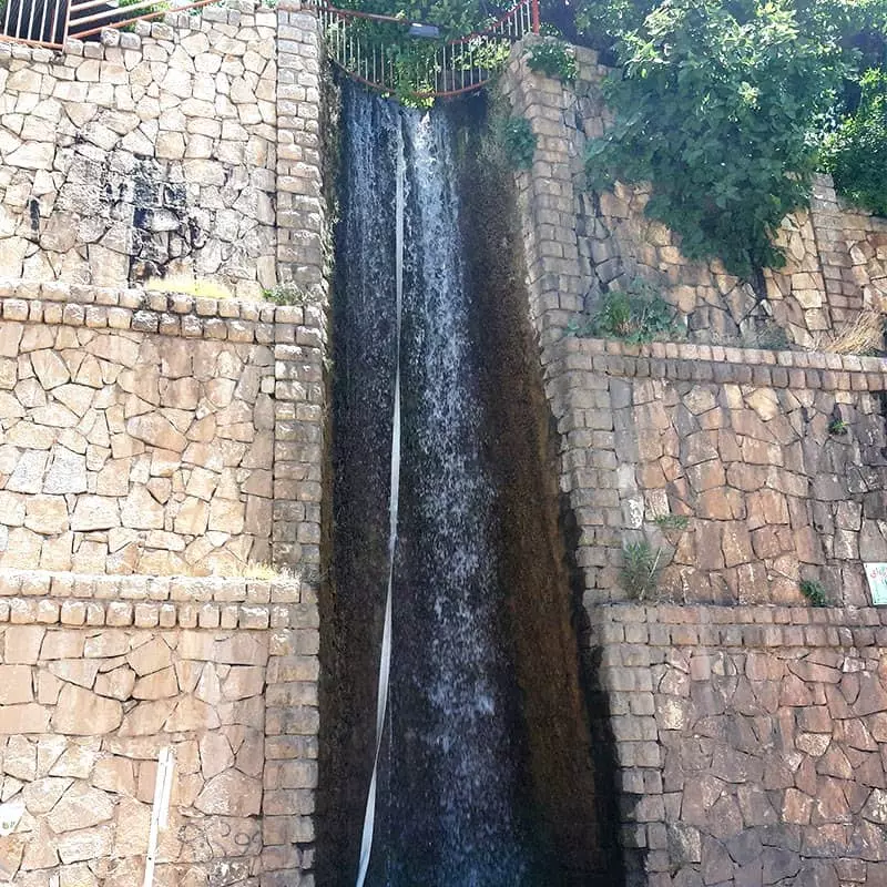 آبشاری بلند در کنار دیواری سنگی