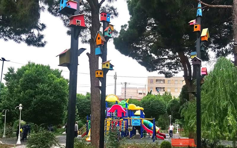 پارکی با شهربازی کودکان و لانه پرنده روی درختان