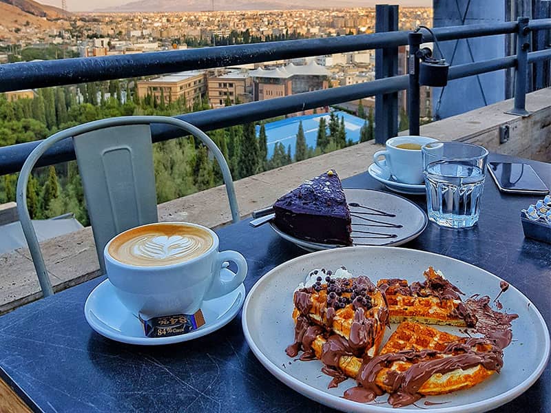 وافل و کیک و قهوه در تراس کافه ای رو به چشم انداز شهر