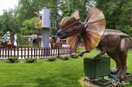 مجسمه دایناسور در محوطه باغ گل ها و زمین بازی کودکان