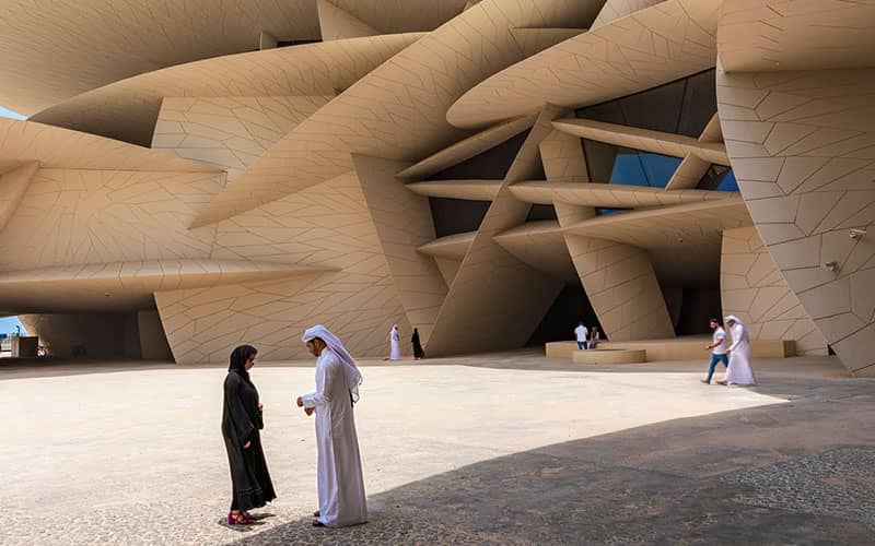 نمای ساختمانی با معماری مدرن و مرد و زنی با لباس عربی در مقابلش
