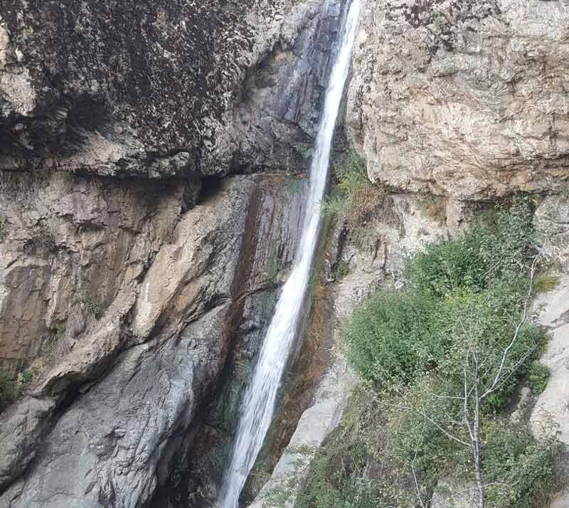 آبشار بلند و باریک سوتک میان صخره های بلند کوه از نمای دور