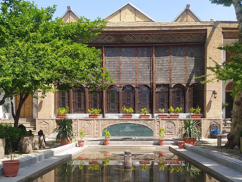 حوض آب در وسط حیاط عمارتی تاریخی با تعداد زیادی پنجره ارسی