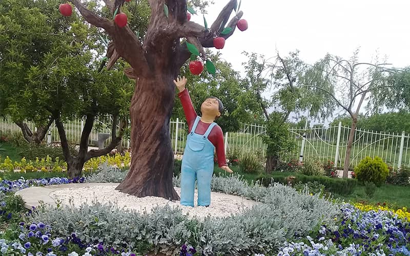 مجسمه کودکی در کنار درخت سیب