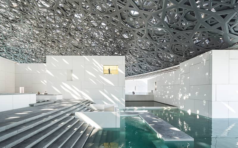 تابش نور خورشید از سقفی توری شکل به داخل ساختمانی سفیدرنگ با پلکان و آب