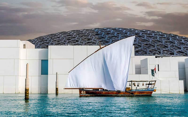 قایقی سنتی در کنار سازه ای با دیوارهای سفید و سقف گنبدی توری شکل