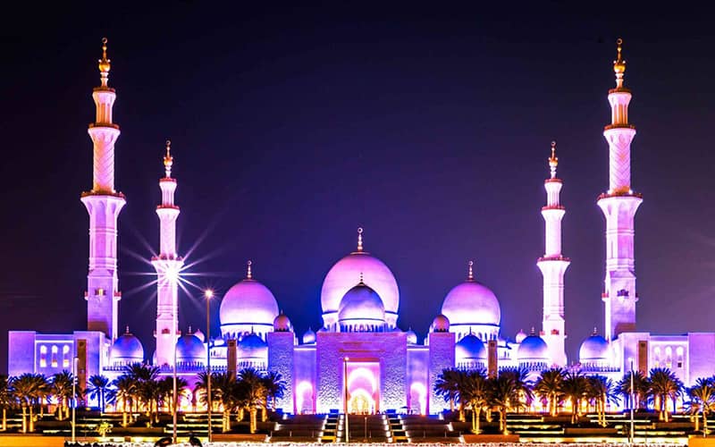 مسجدی با سه گنبد و دو مناره با نورپردازی بنفش در شب