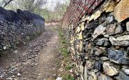 جاده ای خاکی در کنار دیواری سنگی در روستا