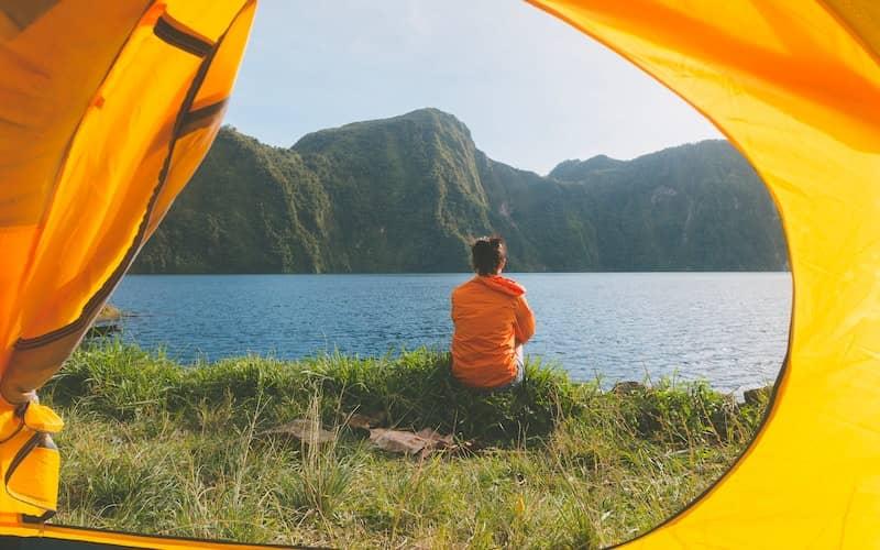 مردی در حال تماشای دریاچه و در کنار چادر کمپینگ