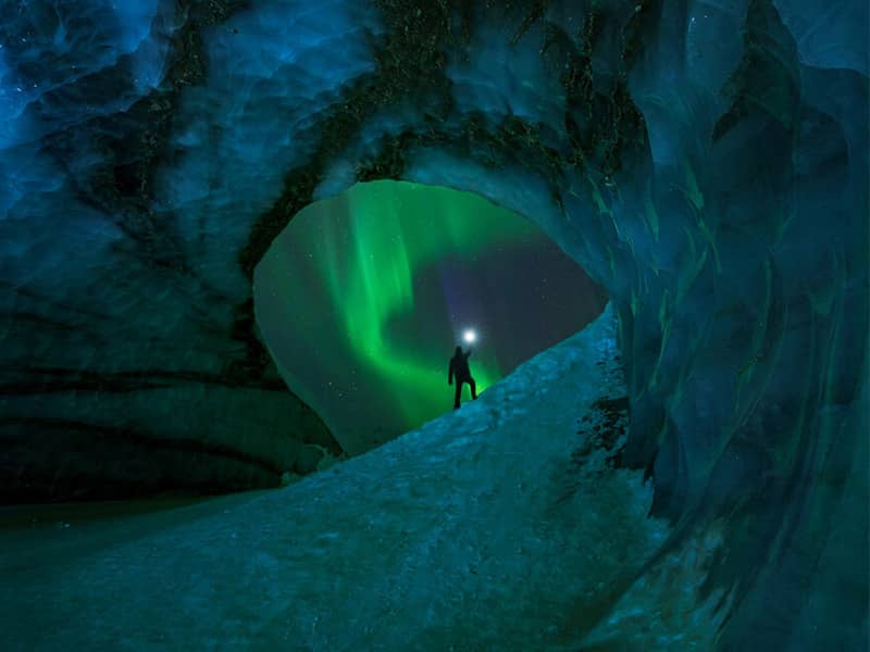 دهانه یک غار برفی با چشم انداز شفق قطبی