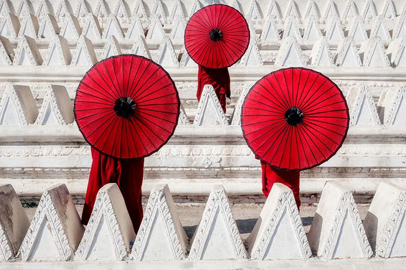 سه نفر با چتر قرمز کنار ساختمان سفید رنگ در میانمار